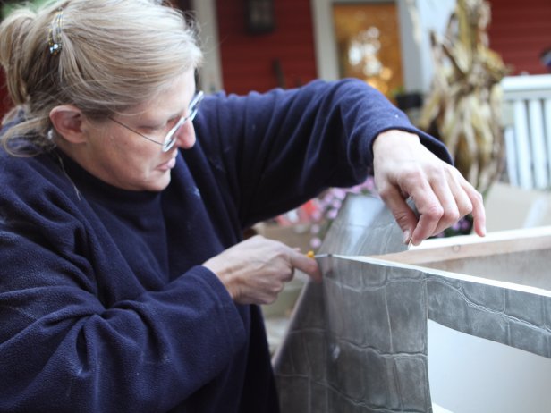 After attaching wallpaper to the base of the vanity, cut away any excess using a utility knife and smooth out air bubbles using a wallpaper smoothing tool.