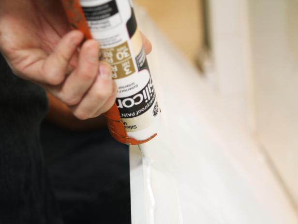 Using a caulk gun, apply silicone adhesive directly to the front of the bathtub.