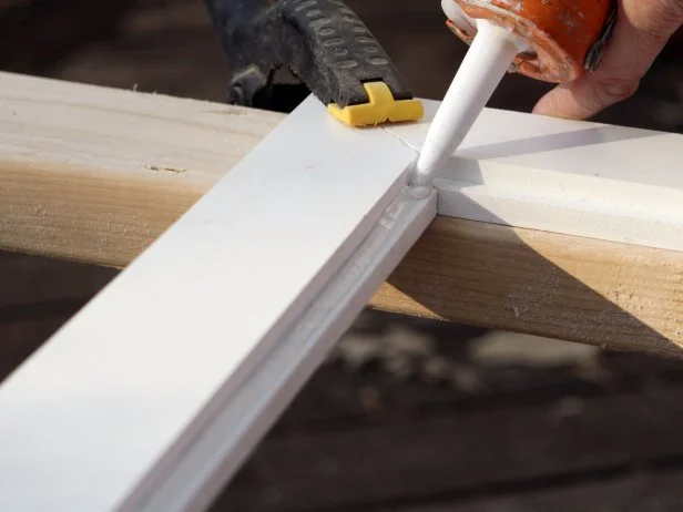 First apply silicone adhesive to the four edges of the beadboard and fit into the grooved trimmed pieces. Attach all four trim pieces with miters lined up. Clamp beadboard panels to trim pieces, let silicone dry for two hours.