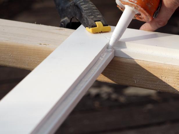 First apply silicone adhesive to the four edges of the beadboard and fit into the grooved trimmed pieces. Attach all four trim pieces with miters lined up. Clamp beadboard panels to trim pieces, let silicone dry for two hours.