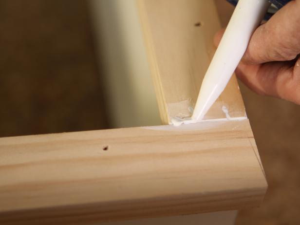 Once all trim is attached to front of bookshelves, fill any nail holes with spackle using putty knife and any gaps with caulk using caulk gun. Wipe away dust with damp cloth to assure clean surface. Sand lightly with medium-grit sanding block, then paint trim same color as bookshelf.