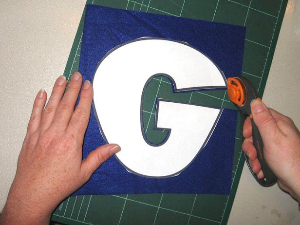 Top view of person cutting around a letter G  on a blue material.