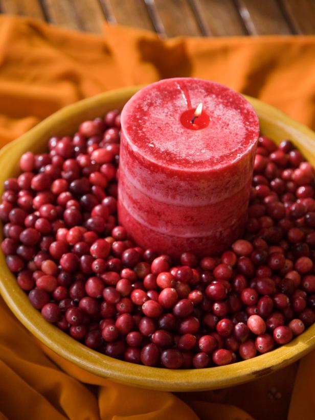 Cranberries in bowl surrounding a red, lit candle. 