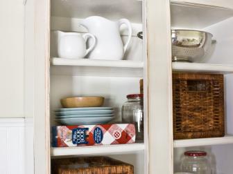 Antiqued white kitchen cabinet with exposed shelves and kitchenware.