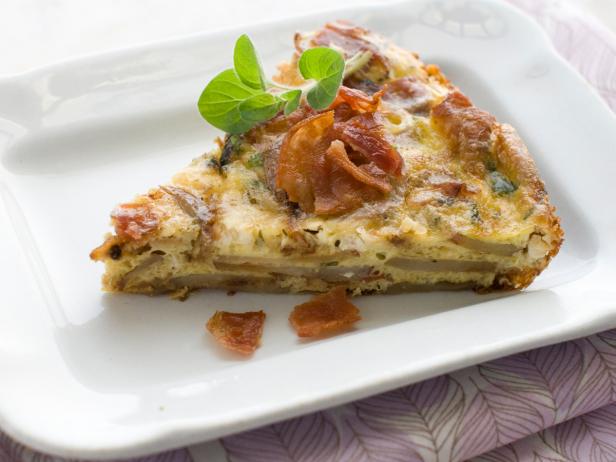 A pie-shaped slice of bacon and potato frittata, garnished with fresh basil, is served at a brunch celebration.