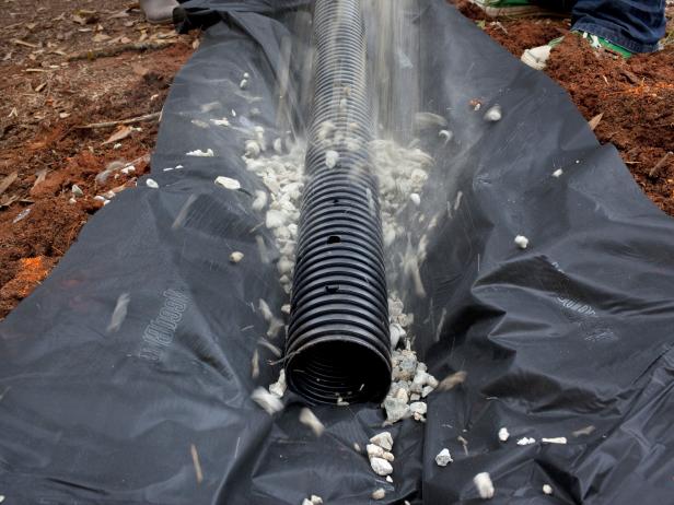 In the next step of building a French drain, place the drain pipe on top of a fabric lining. Add gravel until the pipe is completed covered. There should be 5 inches from the top of the gravel to the ground.