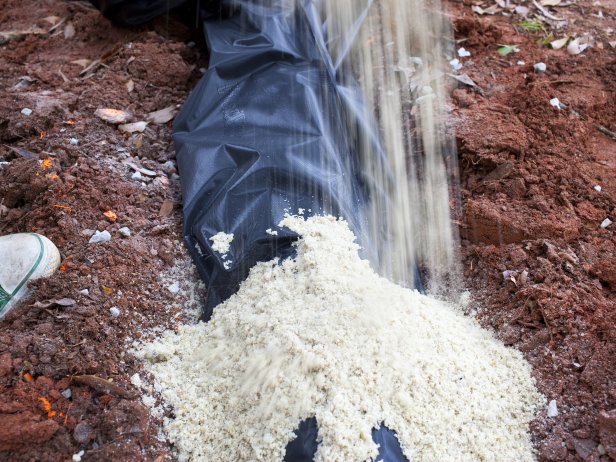 Use shovel to fill trench with sand then topsoil. Cover sand and topsoil with turf and add a bed of stones around open end of drain pipe.