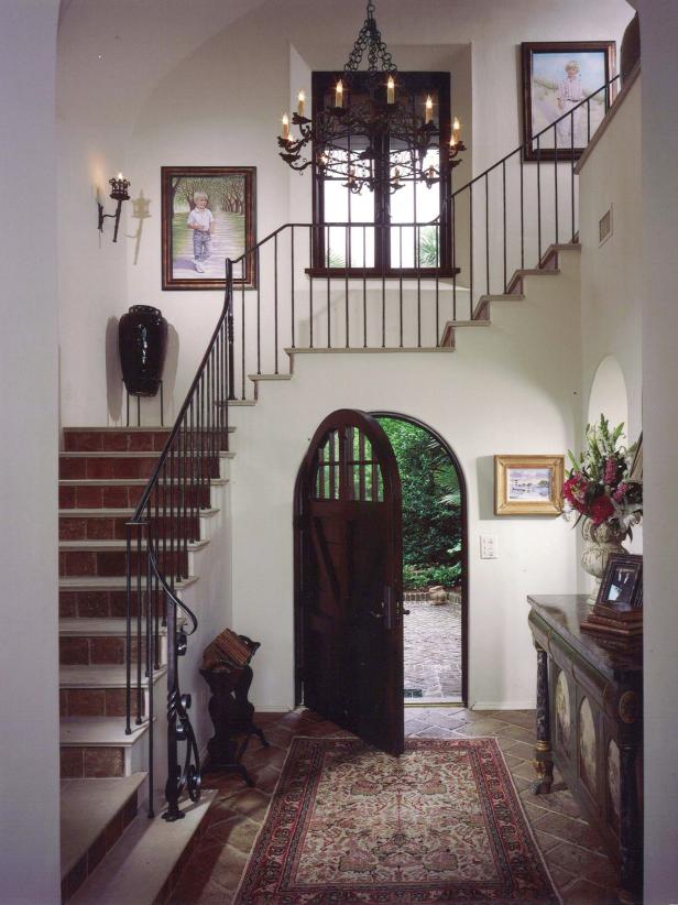 Old World Entryway With Ornate Iron Chandelier and Arched Front Door