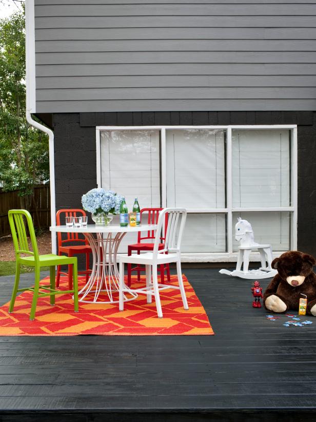 Stained Deck With Colorful Outdoor Rug, Chairs, White Table and Toys 
