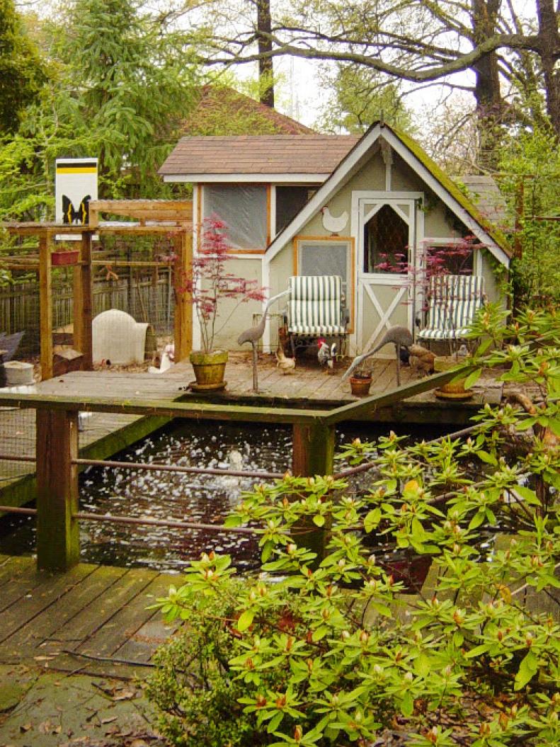 A chicken coop on a square deck near a small pond. 