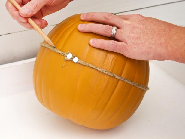 The two thumbtacks should sit right next to each other. Using the yarn or rope as a guide, draw a light pencil line all the way around the pumpkin