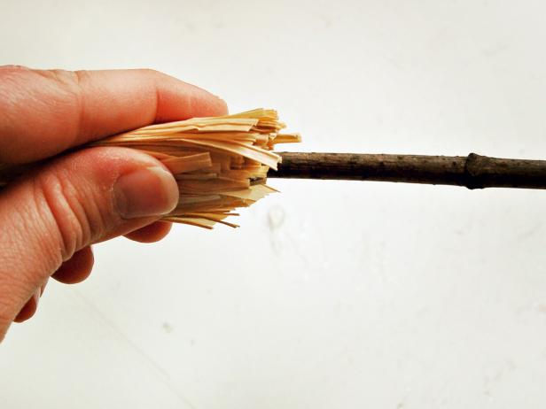 Apply a bead of hot glue around bottom of stick and insert stick into center of raffia bunch, ensuring raffia is evenly distributed around twig. Hold until glue has set.