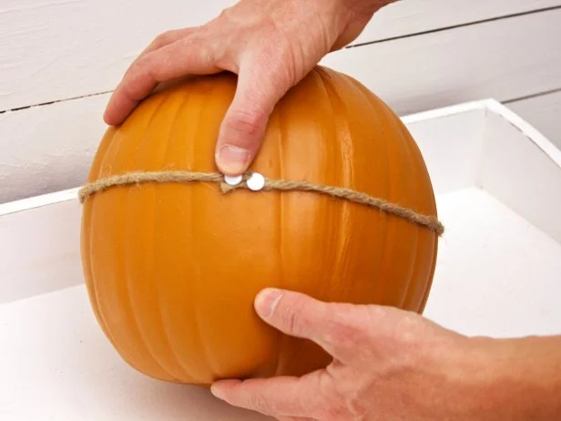 Wrap the yarn or rope all the way around the pumpkin, making sure it stays as level as possible, and secure the other end of it with a thumbtack.