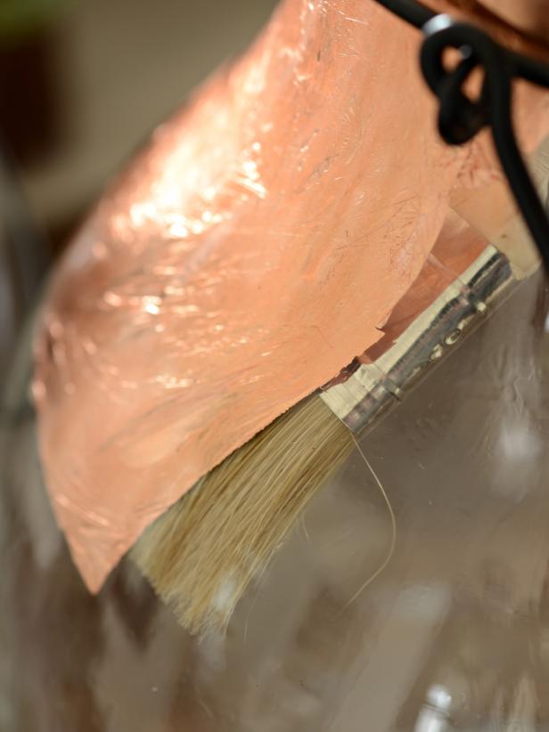 Working from top of the rim down, gently apply full sheets of copper leaf to entire interior of hurricane (Image 1). Smooth down with fingertip or chip brush (Image 2). Continue adding sheets until interior is completely covered. Buff copper with chip brush in a circular pattern to remove excess leaf then empty loosened bits from hurricane. The brush attachment on a vacuum is a great way to remove excess copper leaf. Insert candle or tealight and light as usual. Note: Never leave a burning candle unattended.