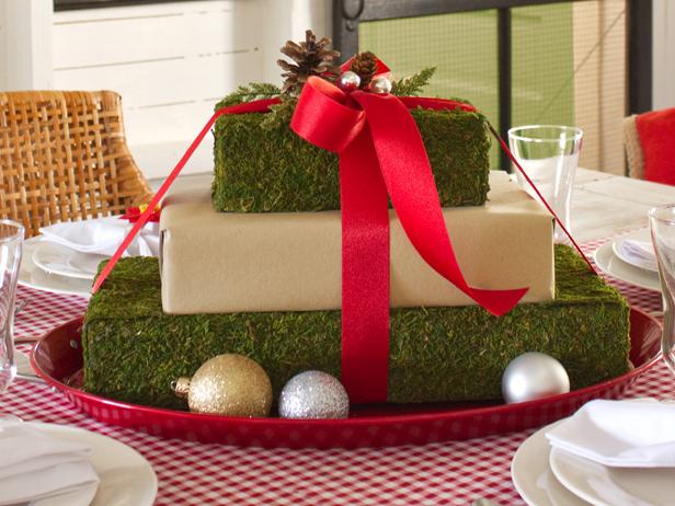 To add finishing touches to a gift box centerpiece, using scissors, cut pieces off of a holiday floral pick, like sprigs of faux greenery, pine cones or metallic silver globes. Affix the pieces atop the bow with hot glue.