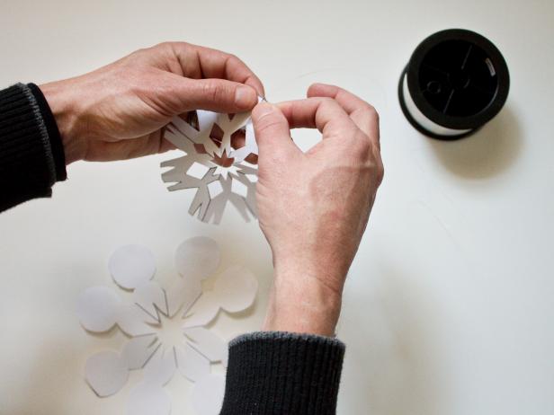 This paper snowflake is attached to fishing line with tape. Use small pieces of transparent tape to attach each of the snowflakes, at various heights, to several lengths of 8 lb. fishing line. Helpful hint: Measure the distance between the inside top of the window frame and the inside bottom of the window frame to determine the correct length of fishing line.