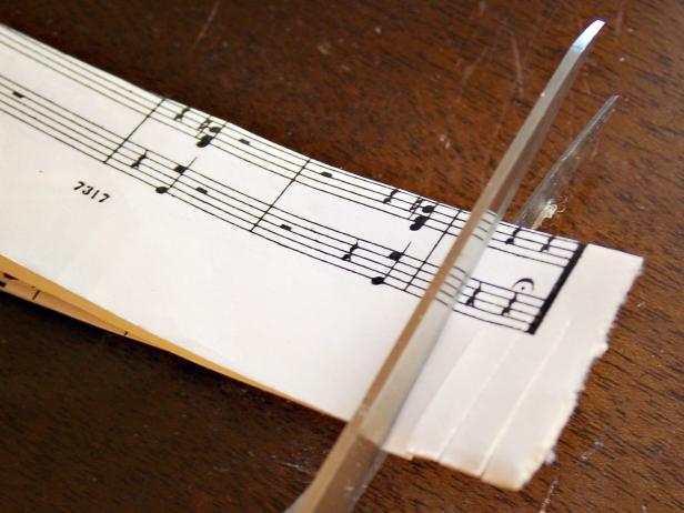 This sheet music strip is being cut with scissors to create fringed edges.