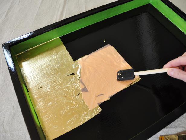 Lay sheets of gold leaf over tray surface, overlapping slightly as necessary. Press into place with a foam brush. Tip: Don't worry about applying gold leaf perfectly. Folds and gaps in the leafing create surface interest.