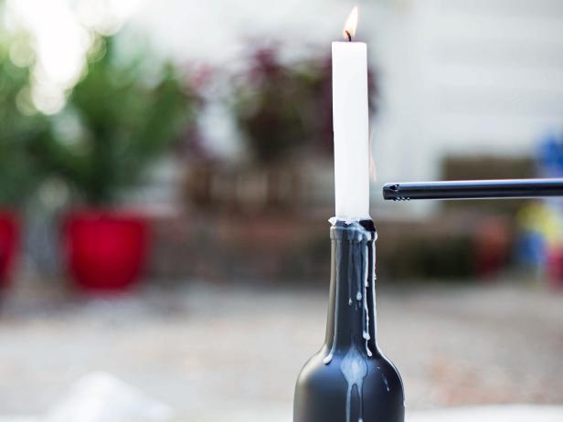 Tapered candles can easily lean then fall off the wine bottles and possibly break. To prevent this, place tapered candles into the openings at the top of each wine bottle, then light wicks immediately. Wax will drip down to the top of the opening, creating a bond between the bottle and the candle and helping each candle stand securely upright. Heavy drips and buildup along the exterior of the bottle adds drama to the overall look. Allow wax to accumulate all the way around the bottle before placing together as a group near your front porch or entryway.
