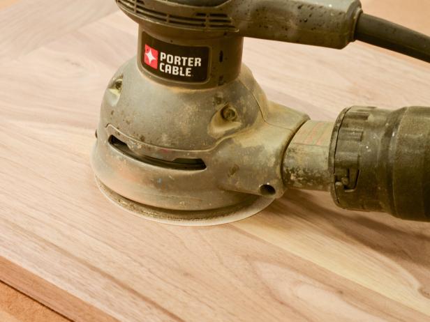 Once glue has dried, remove the cutting board from clamps. Scrape off any excess dried glue gently with a chisel. Using an orbital sander fitted with an 80-grit sanding pad, sand both sides of the board and edges to soften corners. Repeat sanding process with 120-grit, then 220-grit sandpaper. Make sure all dried glue is sanded off surface prior to finishing. Rub entire cutting board with several coats of a food-safe finish like mineral oil, walnut oil or beeswax, allowing oil to fully absorb into the wood. Allow cutting board to dry overnight before use. Tip: Most food-safe finishes need to be reapplied regularly. If giving this board as a gift, also present the recipient with a bottle of oil as a companion gift along with care instructions.