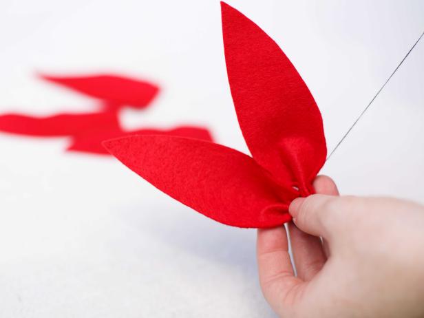 While creating a felt poinsettia, use a needle and spool of thread to attach each of the cut-out felt leaves together.
