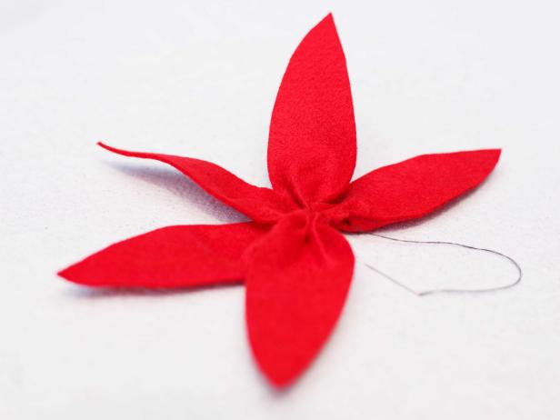 As several felt poinsettia leaves are stitched together, ensure a snug fit by pulling the thread tight and checking the bottom tip of each leaf for proper, consistent bunching.