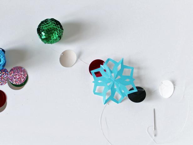 To create the garland, string a 30-inch piece of monofilament onto the sewing needle. Start with the sequin ball by threading the monofilament through a top section of it. Then, thread on some color sequins and snowflakes in a random pattern. Tip: Keep a few inches of monofilament between each decoration to help the garland look more natural when you’re done.