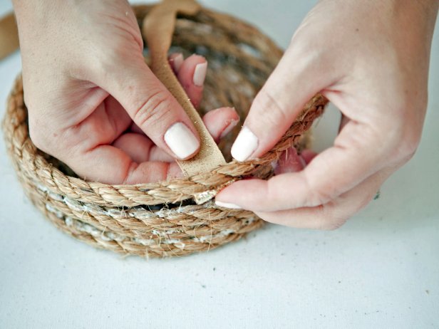 To add ribbon to the sides of your rope basket, after a few rows of height, glue the ribbon onto the underside of the rope. Wrap the ribbon around the rope about 5 times. Glue the end of the ribbon to the underside of the rope.