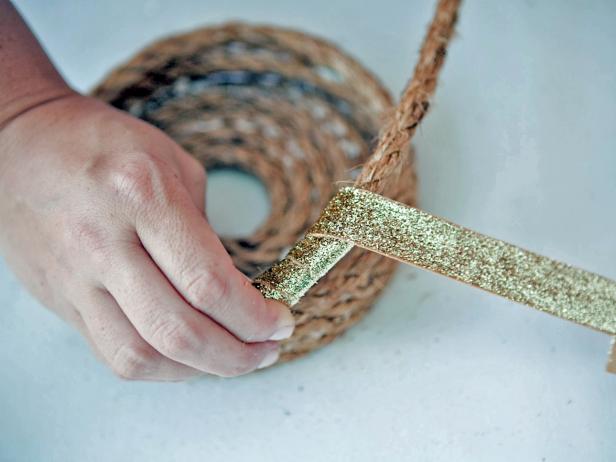 To add metallic ribbon to your rope basket, after building up a few rows of height, glue the ribbon onto the underside of the rope. Wrap the ribbon around the rope about 5 times. Glue the end of the ribbon to the underside of the rope.