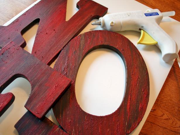When your letters are completely dry, arrange them how you want on a piece of cardboard. Place another piece of cardboard on the front of the letters to help flip them over. Now you are ready to glue your letters in place. Take your glue gun and fill all the gaps with hot glue.