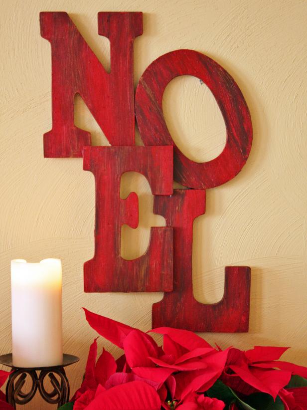 Red Wooden Letter Holiday Sign Above Red Poinsettias and White Candle