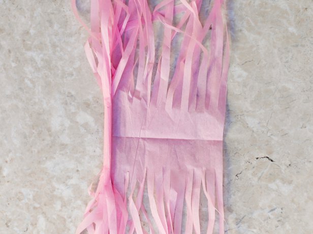 To create the tassels for the hanging garland, unfold tissue paper. Begin rolling tightly down the middle crease. Continue rolling, fold in half and then twist to create a loop for hanging.