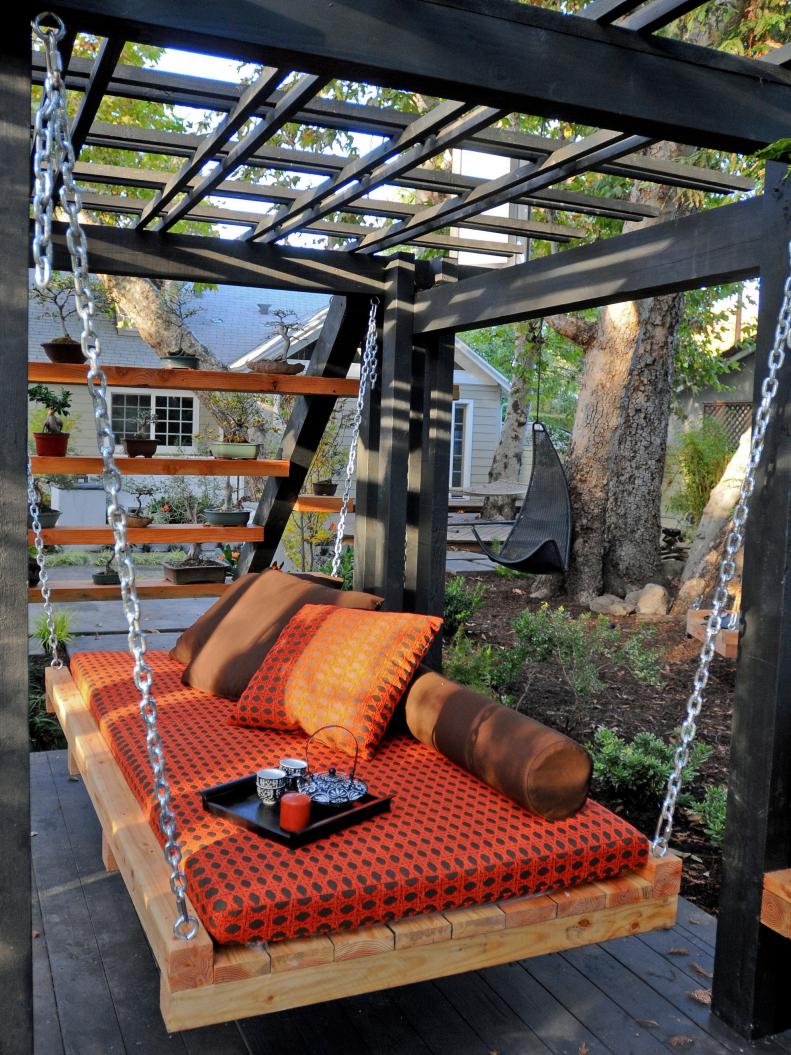 Black Wood Deck With Pergola and Suspended Daybed With Red Cushions