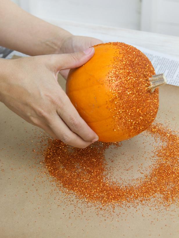 Pick up the pumpkin and shake off any glitter that didn't fully adhere. Set the pumpkin aside and fold the craft paper to funnel the excess glitter back into its original container.