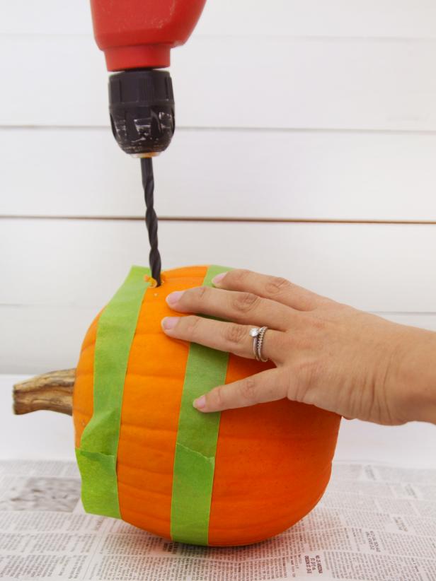 Use a large drill bit to drill holes into the pumpkin just under the top piece of painter's tape.