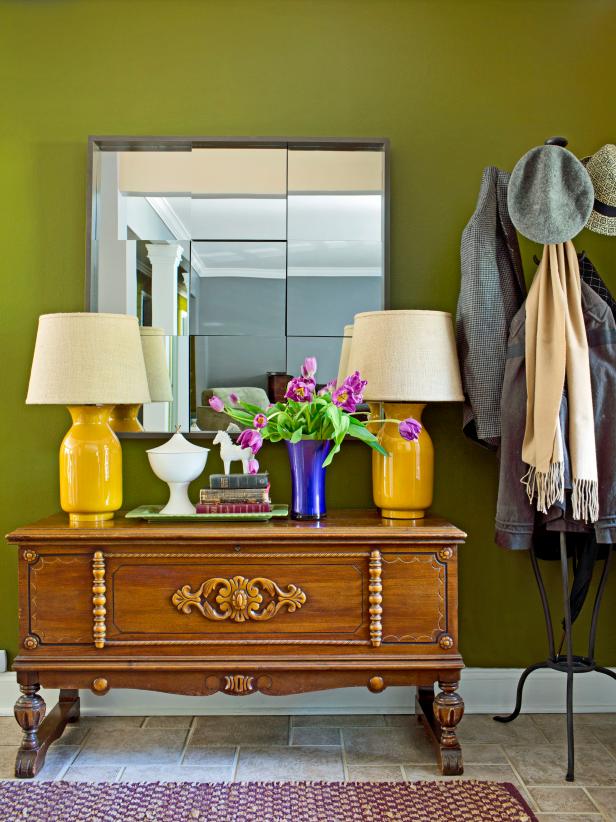 Once you've finished and hung up your homemade mirror project, all that remains is to stand back and admire your handiwork. Here, the mirror has been hung on a green wall and positioned behind a side table on which are two yellow lamps, a bouquet of magenta flowers and a small green tray.