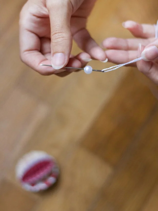 Use a sewing needle to thread a 8&quot;-10&quot; piece of thin twine through a craft pearl or decorative bead.