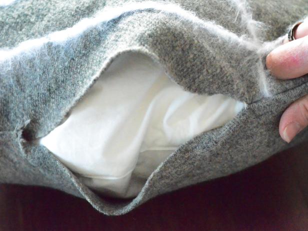 Gently insert pillow form in cover, making sure it fills cover to each corner. Fold raw edges of opening inside pillow cover and pinch together, pinning it shut. Use a whipstitch to sew edges closed with an all-purpose sewing needle and dark gray all-purpose cotton thread. Remove pins and trim any loose threads.