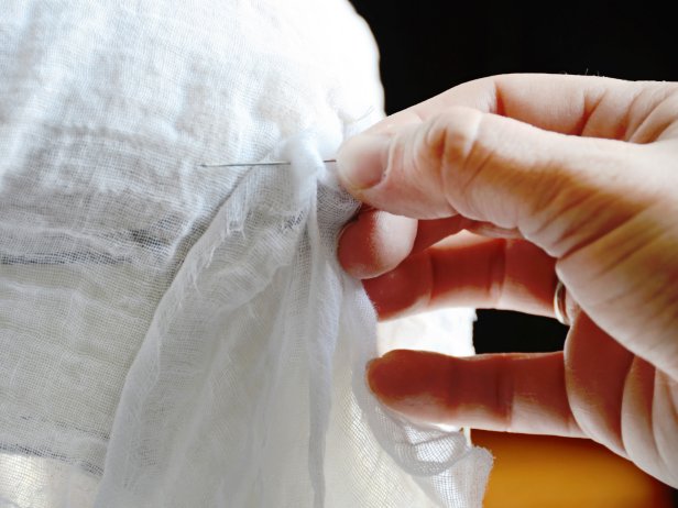 Using an all-purpose sewing needle threaded with white cotton thread, hand-stitch cheesecloth to slipcover in two or three places per strip (Image 3). Trim all excess threads.