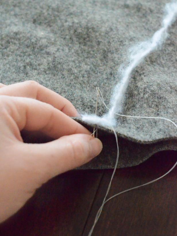 With a sewing needle and all-purpose white thread, tack yarn into place at the pillow's edges and center point.