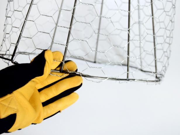 Put on work gloves and roll out chicken wire, then gently wrap wire around lampshade frame to estimate how much is needed to fully cover sides.