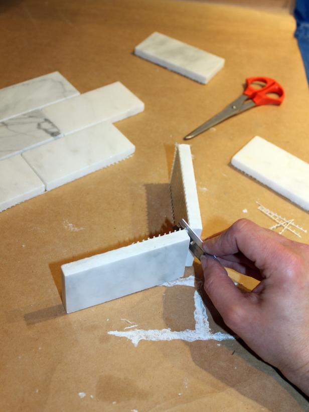 Applying full sheets of mesh-backed tile to the wall can be tricky around outlets or other obstacles, so it's easiest to cut apart and set individual tiles around these. Using a razor blade or scissors, cut tiles away from the mesh backing.