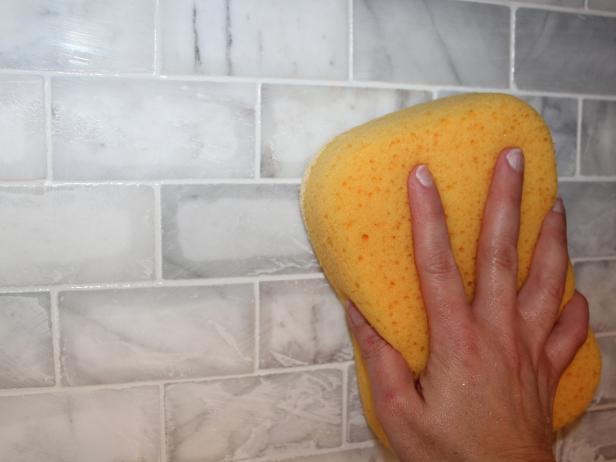 Using circular motions, clean the tile surface with a damp grout sponge, frequently rinsing and wringing it out in the sink.