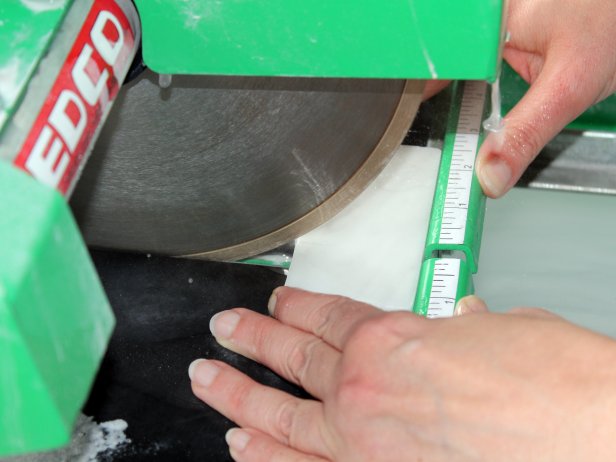 Turn on the wet tile saw, allowing water to coat the blade. Position tile so the blade will hit on your marked line and slowly move tile through the saw.