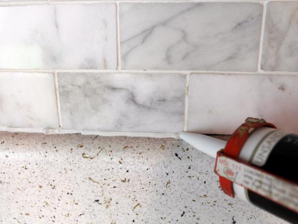 Load caulk into caulking gun and cut off the tip at a slight angle. Position tip in the gap between countertop and tile. While applying even pressure, slowly move caulk gun along seam, leaving a line of caulk.