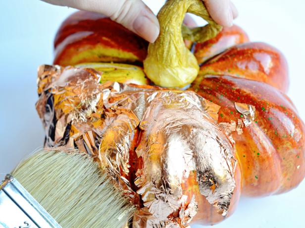 After applying metallic leaf to the pumpkin, smooth down the leaf with your fingertip or a chip brush. Repeat this process until all raised areas on the pumpkin are leafed.