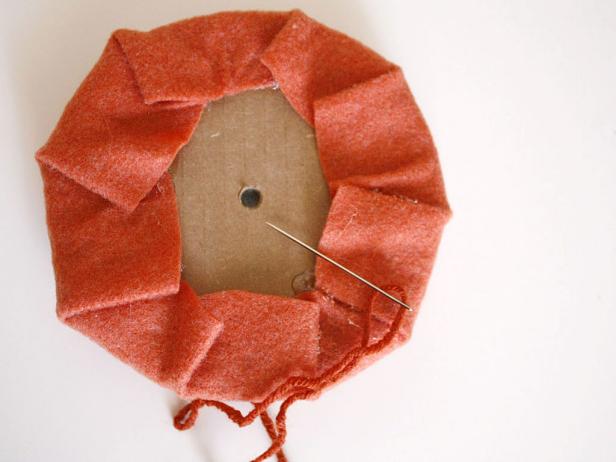 Poke a hole in the center of the cardboard, then thread a needle with orange yard to create seams on your pumpkin.