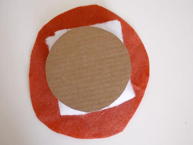 To create the pumpkin shape, stack a circle of felt plus two layers of quilt batting and the cardboard circle together. Glue in place.