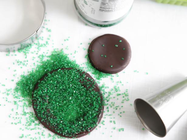 Lightly coat the chocolate fondant circle with water and sprinkle with green sanding sugar to create the wreath.
