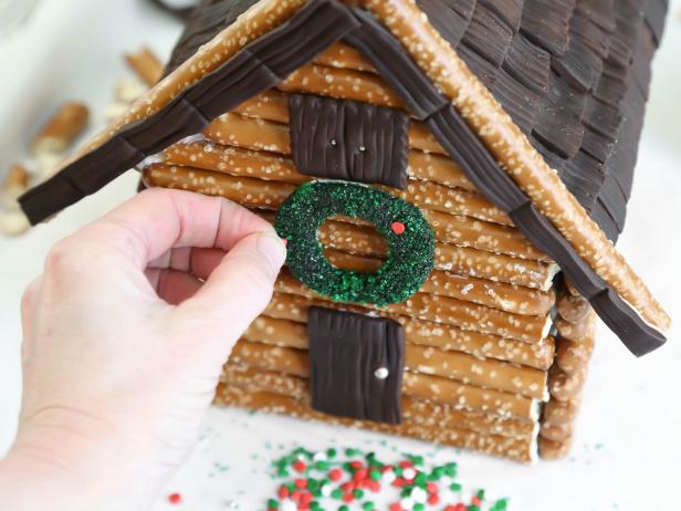 For an adorable finishing touch on a log cabin-style gingerbread house, adhere a chocolate fondant wreath just above the front door using royal icing. Press in confetti sprinkles onto wreath.